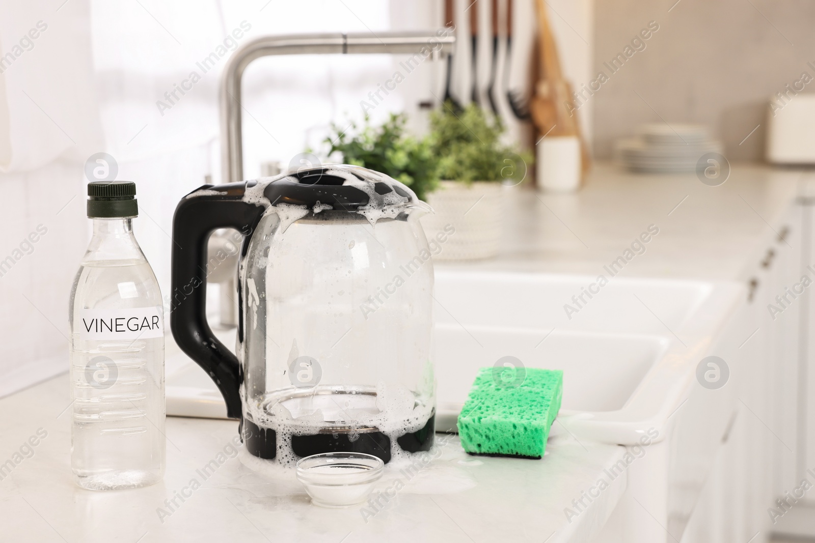 Photo of Cleaning electric kettle. Bottle of vinegar, sponge and baking soda on countertop in kitchen