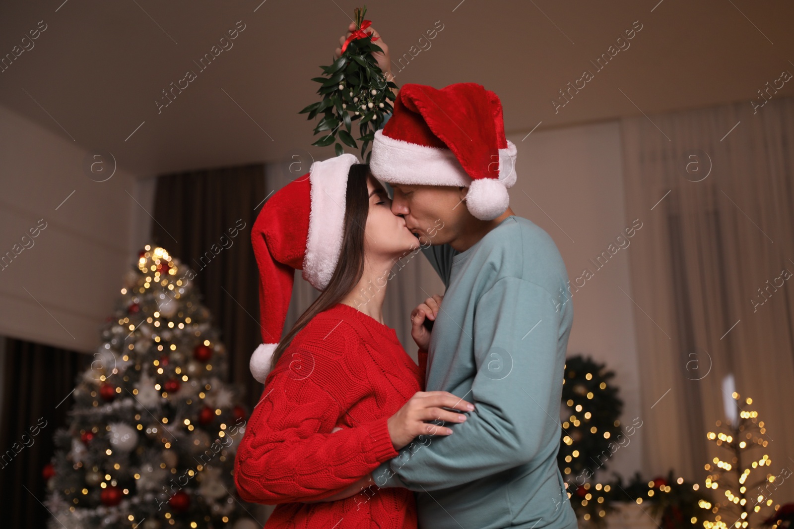 Photo of Couple kissing under mistletoe in room decorated for Christmas