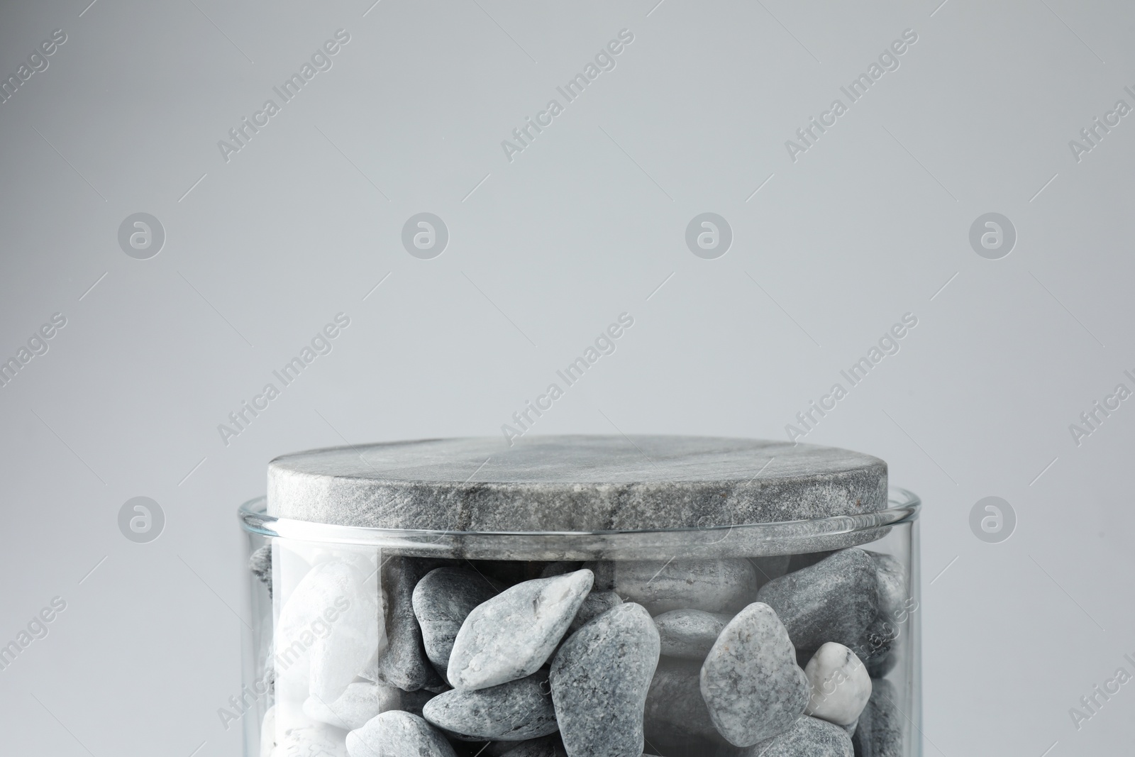 Photo of Presentation for product. Glass container with stones on light grey background. Space for text