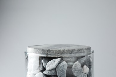 Photo of Presentation for product. Glass container with stones on light grey background. Space for text