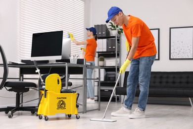 Cleaning service workers cleaning in office. Bucket with wet floor sign indoors
