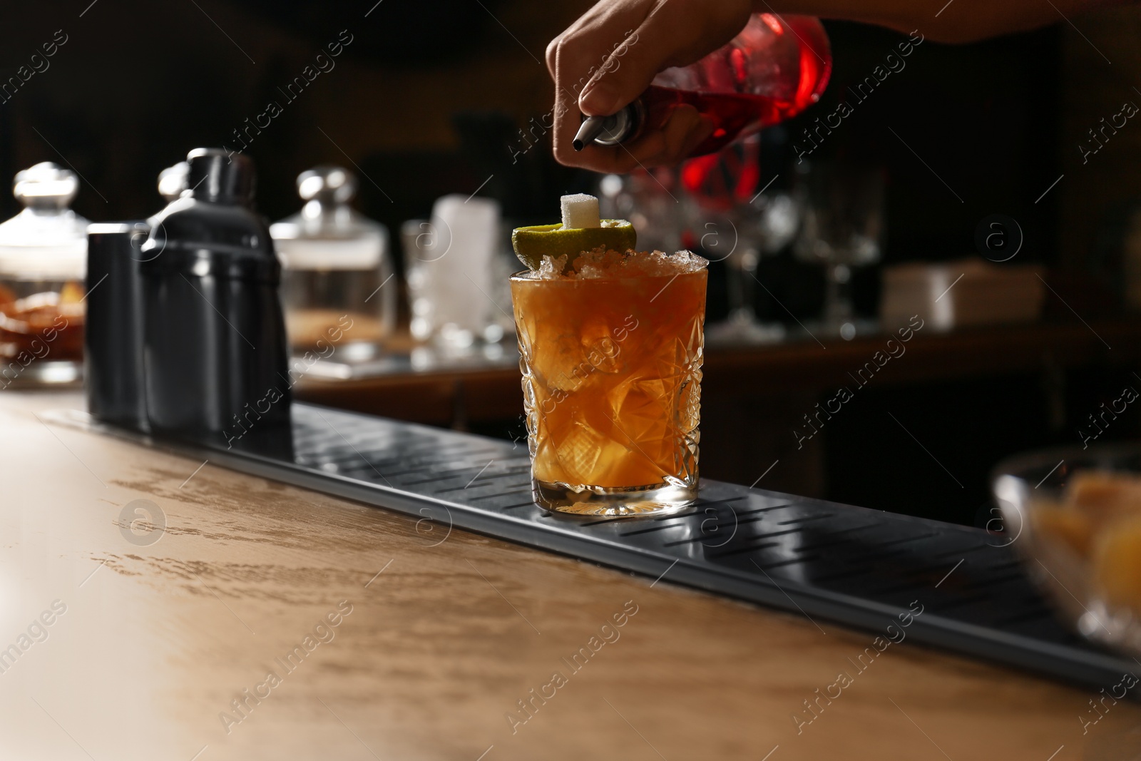 Photo of Bartender decorating glass of fresh alcoholic cocktail at bar counter, closeup