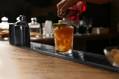 Photo of Bartender decorating glass of fresh alcoholic cocktail at bar counter, closeup