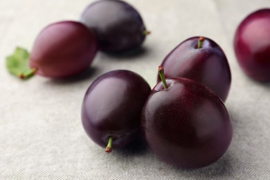 Photo of Many tasty ripe plums on light fabric, closeup