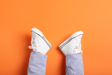 Photo of Little baby in stylish gumshoes on orange background, top view. Space for text