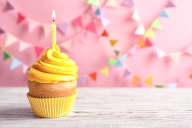 Photo of Delicious birthday cupcake with burning candle on table