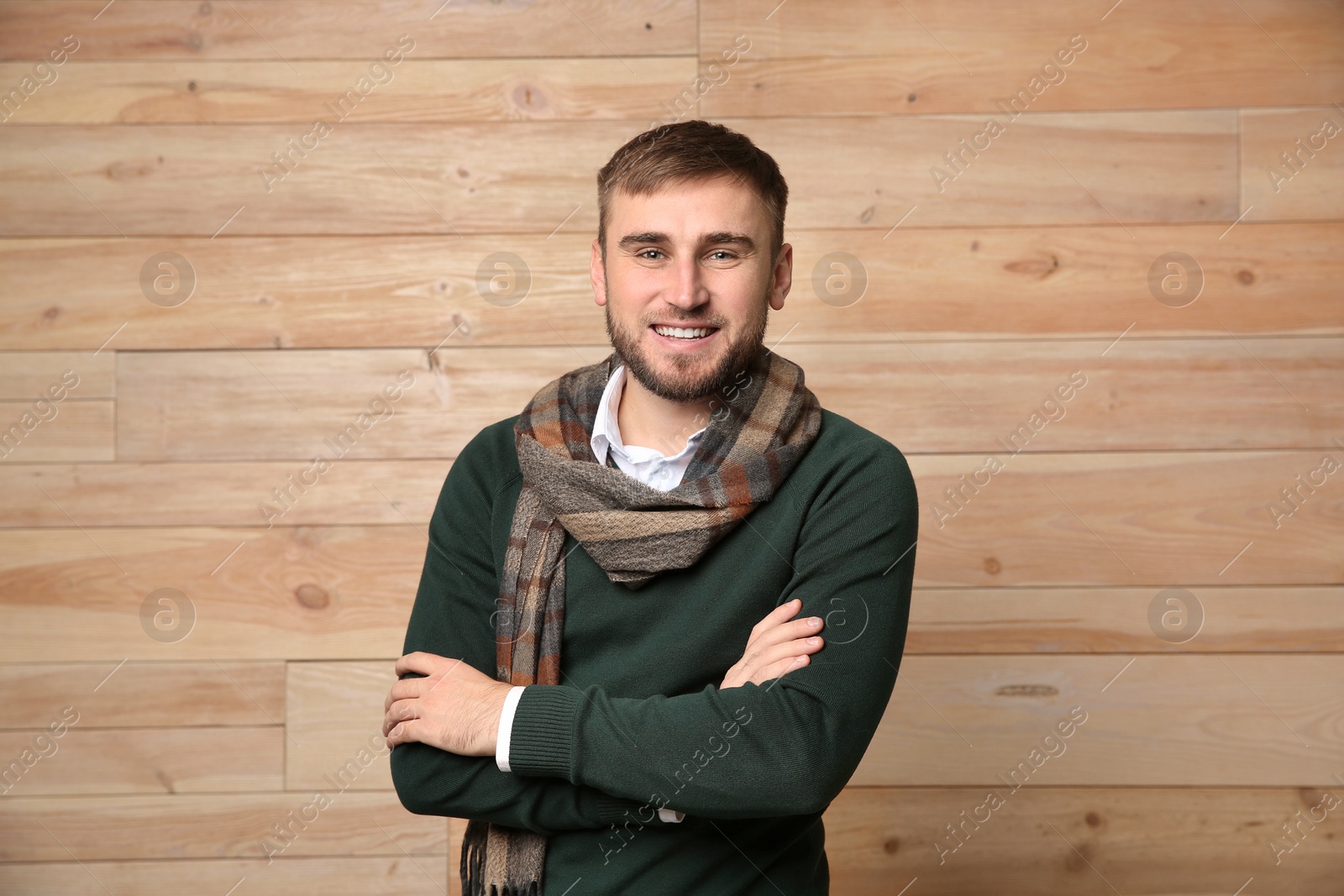 Photo of Handsome young man in warm sweater with scarf on wooden background