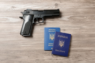 Gun with Ukrainian passports on wooden background, flat lay