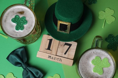 St. Patrick's day party on March 17. Green beer, leprechaun hat, bowtie, wooden block calendar and decorative clover leaves on green background, flat lay