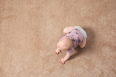 Cute little baby crawling on carpet indoors, top view with space for text