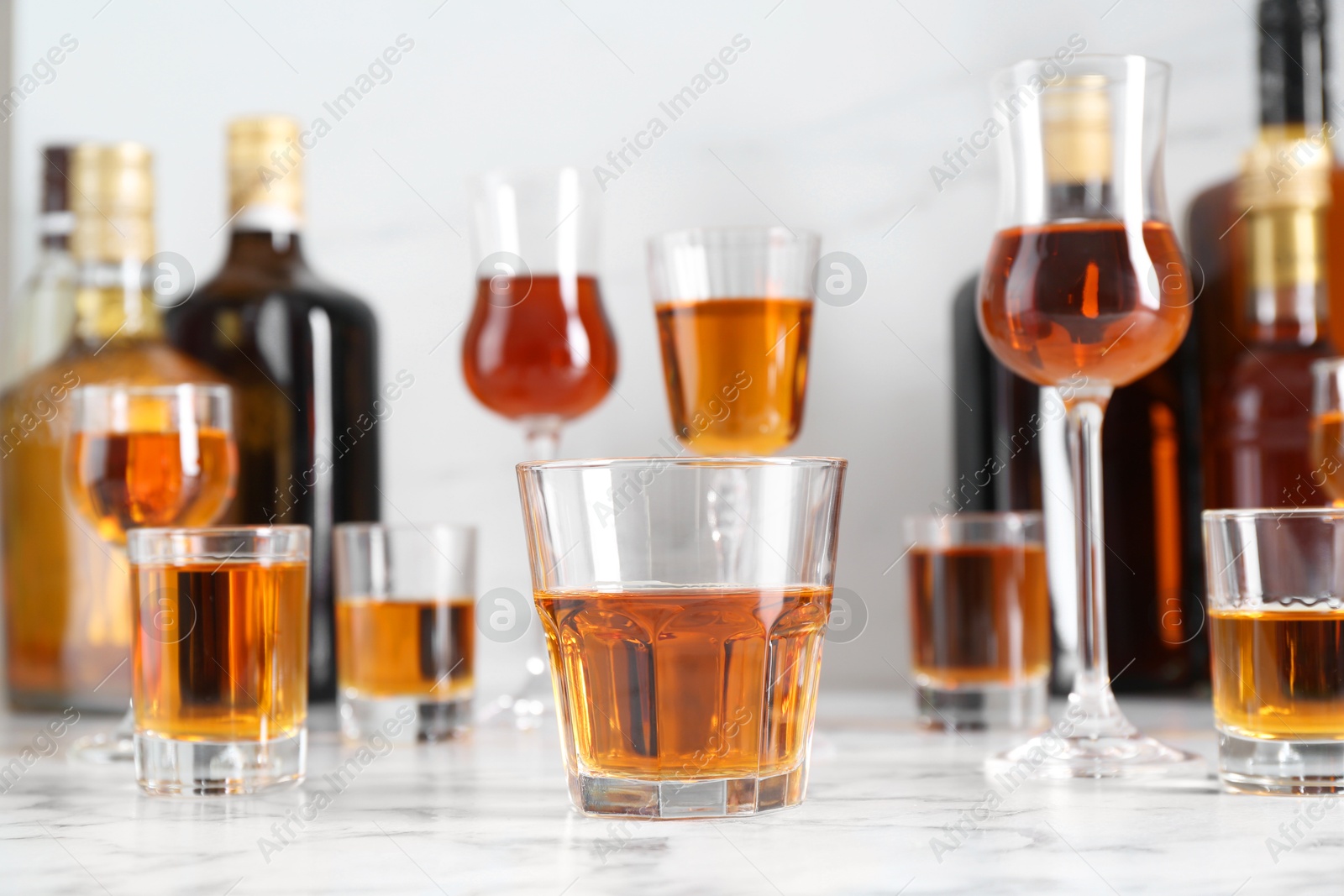 Photo of Delicious liqueurs in glasses and bottles on white marble table