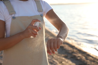 Young woman using insect repellent on beach, closeup