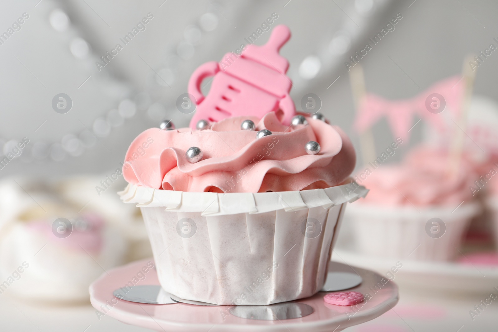 Photo of Delicious cupcake with pink cream and topper for baby shower on stand, closeup