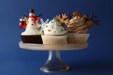 Dessert stand with tasty Christmas cupcakes on blue background