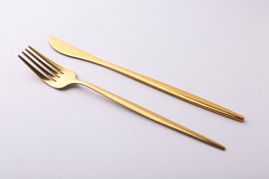Photo of Stylish cutlery. Golden knife and fork on gray background