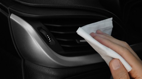 Photo of Man cleaning air vent with wet wipe in car, closeup. Protective measures