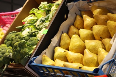Photo of Many fresh pears and broccoli in containers at market