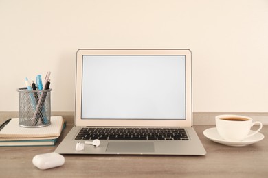 Photo of Modern laptop with blank screen, earphones and coffee on table in office