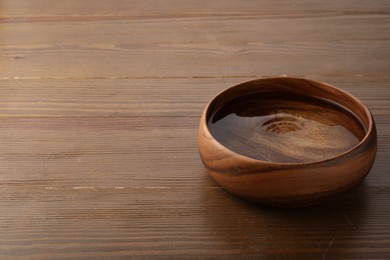 Bowl with clear water on wooden table. Space for text