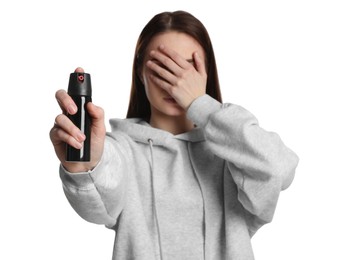 Young woman covering eyes with hand and using pepper spray on white background