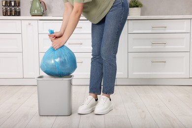 Photo of Woman taking garbage bag out of trash bin in kitchen, closeup