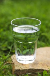 Photo of Glass of fresh water on stone in green grass outdoors