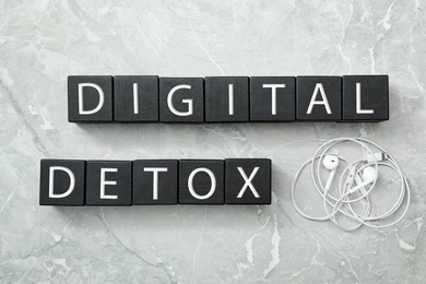 Photo of Black cubes with words DIGITAL DETOX and earphones on light grey marble background, flat lay