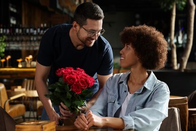 International relationships. Handsome man presenting roses to his beloved woman in cafe