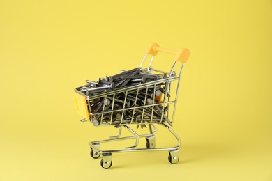 Photo of Metal nails in shopping cart on yellow background