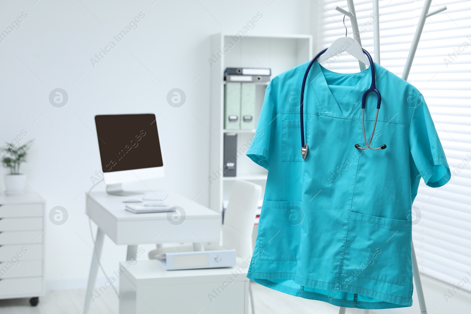 Photo of Turquoise medical uniform and stethoscope hanging on rack in clinic. Space for text