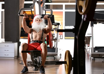 Young muscular man in Santa costume training at gym