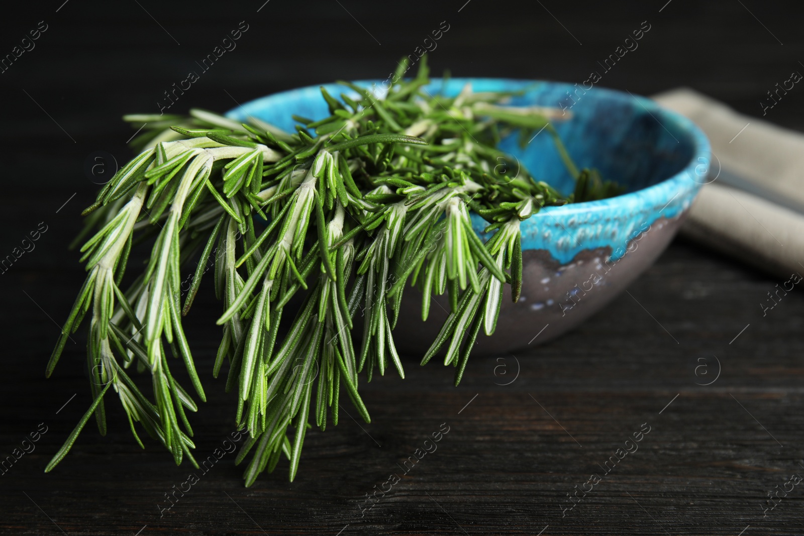 Photo of Bowl with fresh rosemary twigs on wooden table