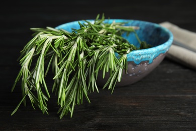 Bowl with fresh rosemary twigs on wooden table