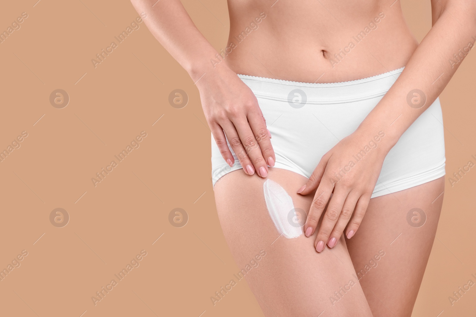 Photo of Woman with smear of body cream on her leg against light brown background, closeup. Space for text