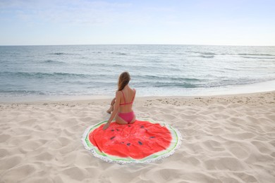 Photo of Beautiful woman sitting on beach towel near sea, back view