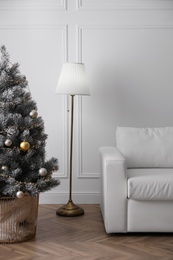 Photo of Christmas tree near sofa against in room. Interior design