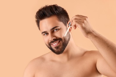 Handsome man applying cosmetic serum onto face on beige background