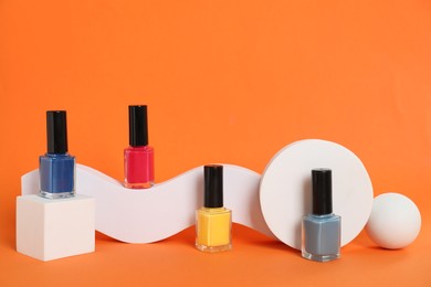 Photo of Stylish presentation of bright nail polishes in bottles on orange background