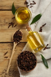 Photo of Essential oil and dried cloves on wooden table, flat lay