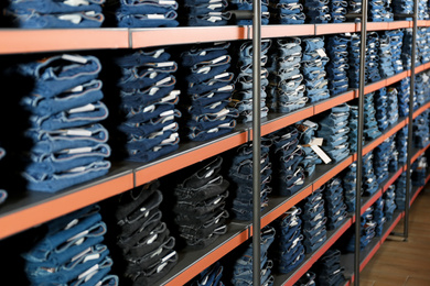 Photo of Collection of stylish jeans on shelves in shop