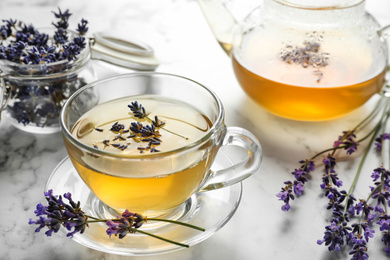 Photo of Fresh delicious tea with lavender and beautiful flowers on white marble table