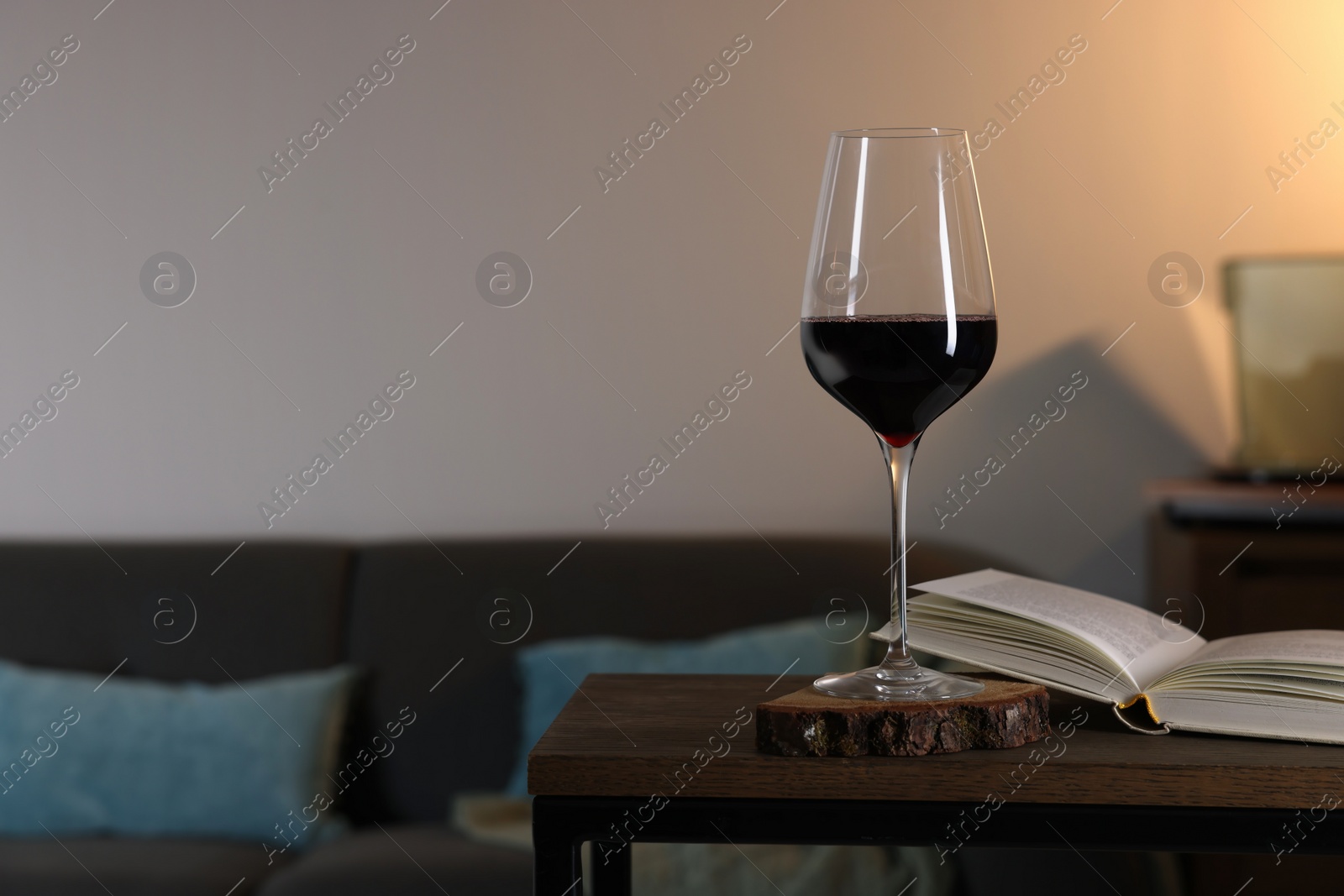 Photo of Glass of red wine and open book on wooden table in room, space for text. Relax at home