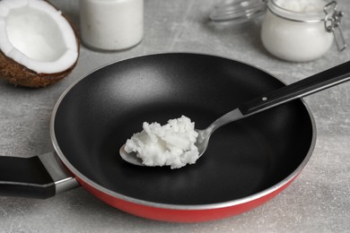 Photo of Frying pan with coconut oil and spoon on light grey table