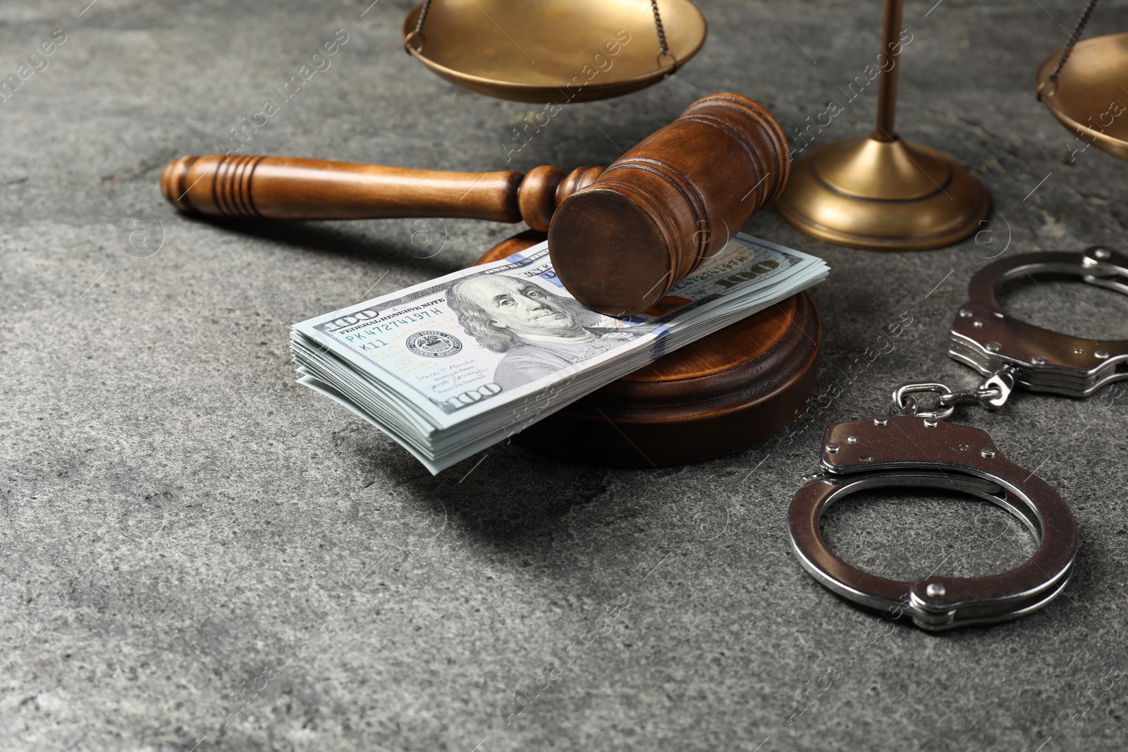 Photo of Judge's gavel, money, handcuffs and scales of justice on grey table
