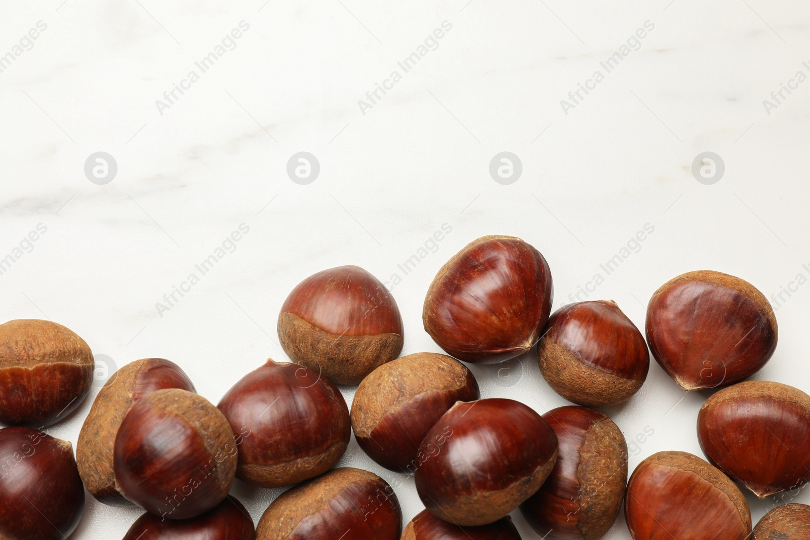Photo of Sweet fresh edible chestnuts on white marble table, top view. Space for text
