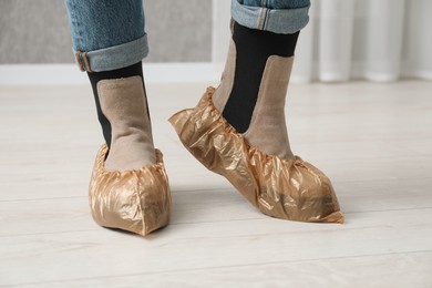 Photo of Woman wearing shoe covers onto her boots indoors, closeup
