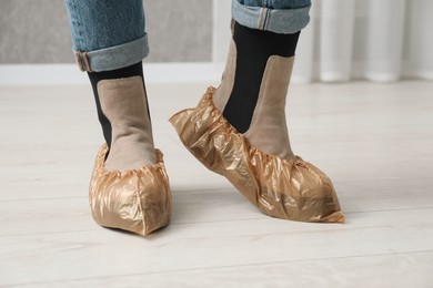 Woman wearing shoe covers onto her boots indoors, closeup