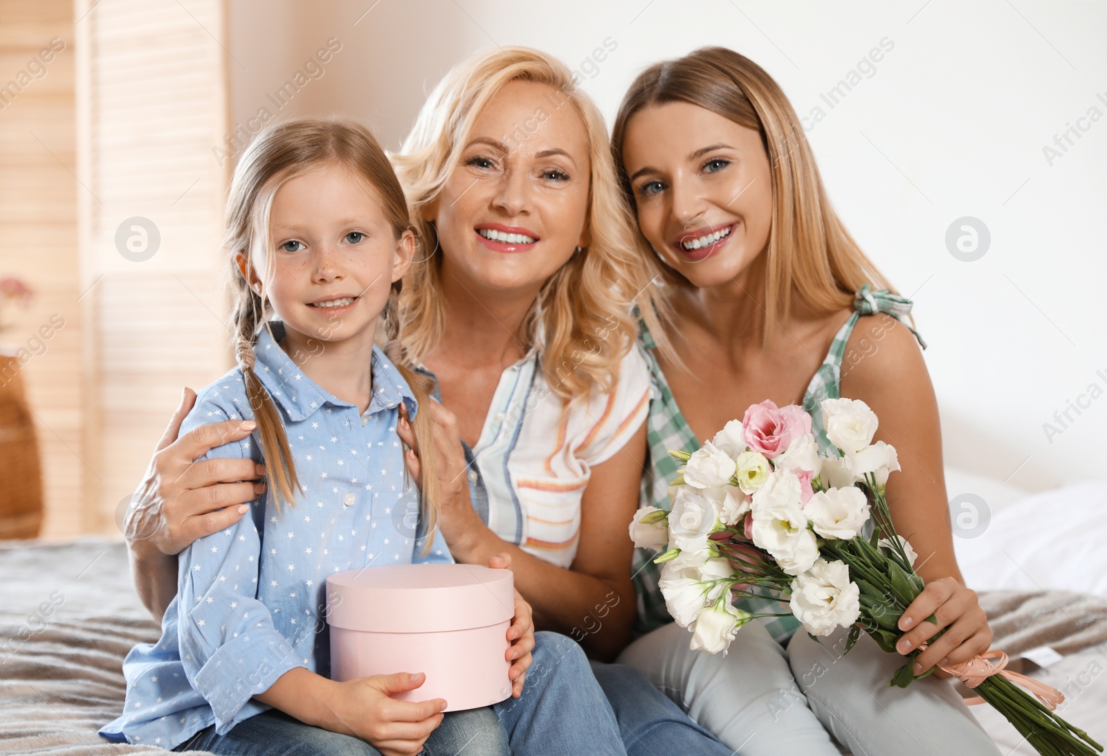 Photo of Young woman with her mature mother and little daughter in bedroom. Holiday celebration