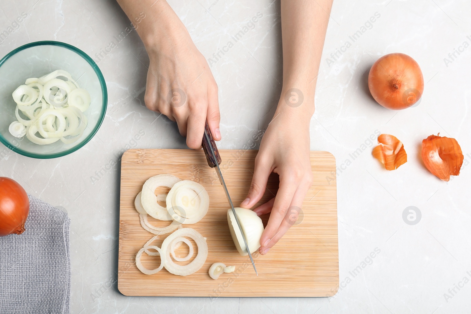 Photo of Woman cutting onion on wooden board, top view