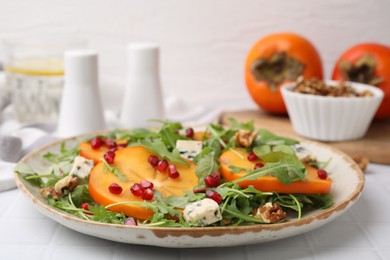 Tasty salad with persimmon, blue cheese, pomegranate and walnuts served on white tiled table, closeup